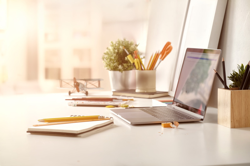 Office environment with desk with laptop, note pad and pencils.