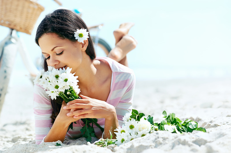 Woman practicing self-love relaxing on the beach holding daisies