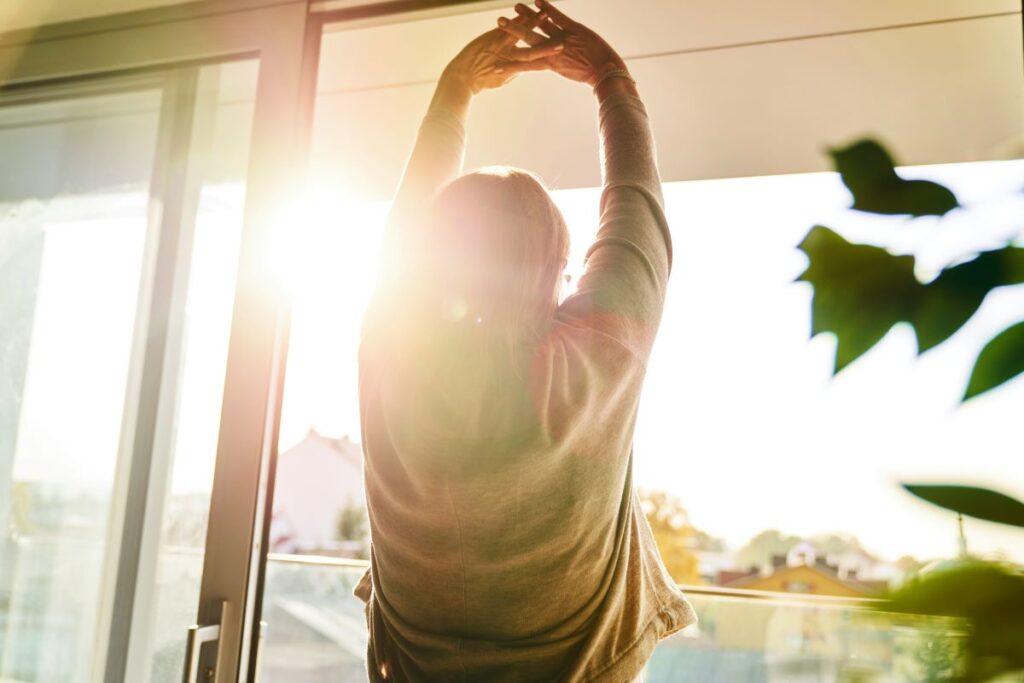 Woman practicing self-love with the sun on her face and stretching