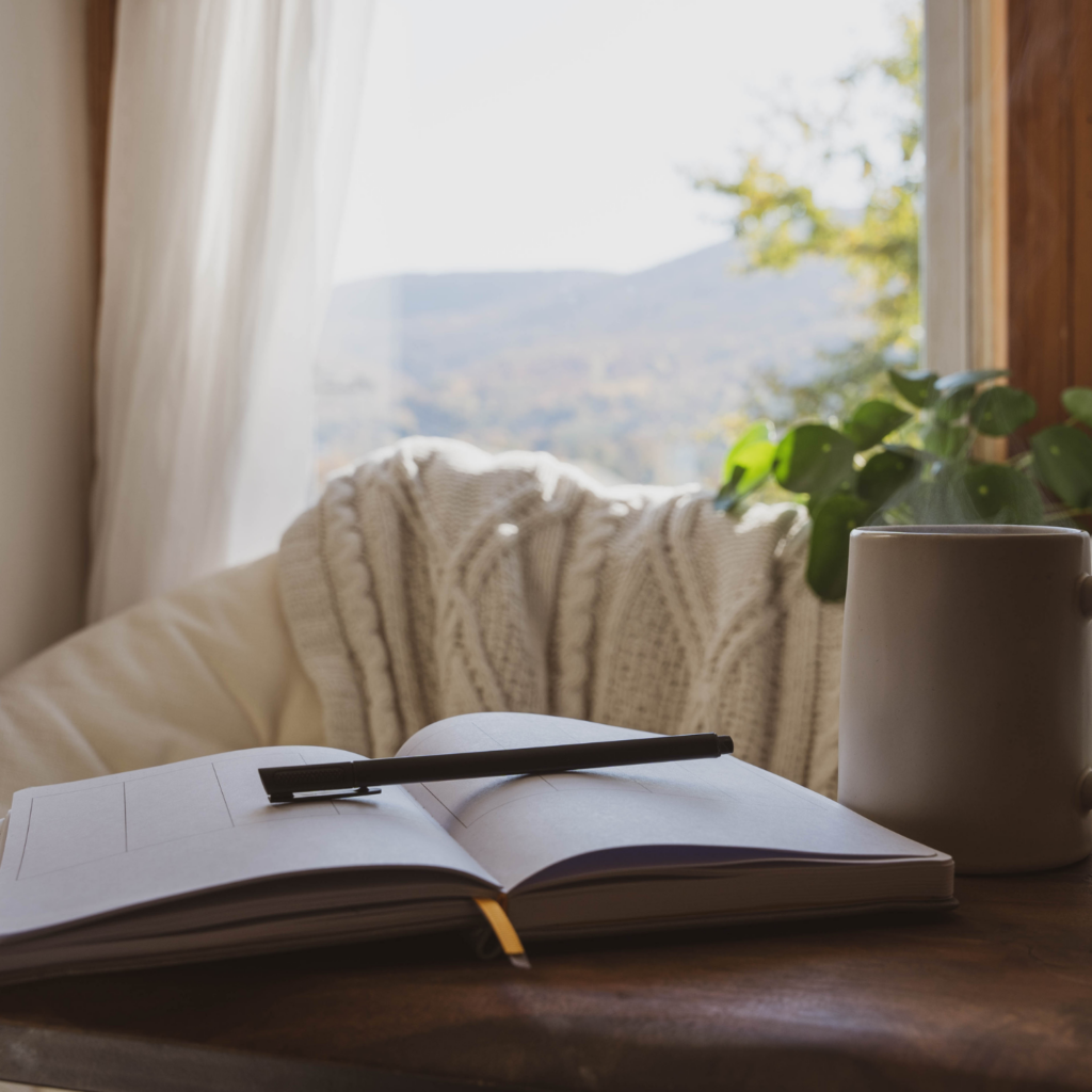 A cozy window nook with an open journal and a steaming cup of coffee, perfect for daily holiday self-care for moms.