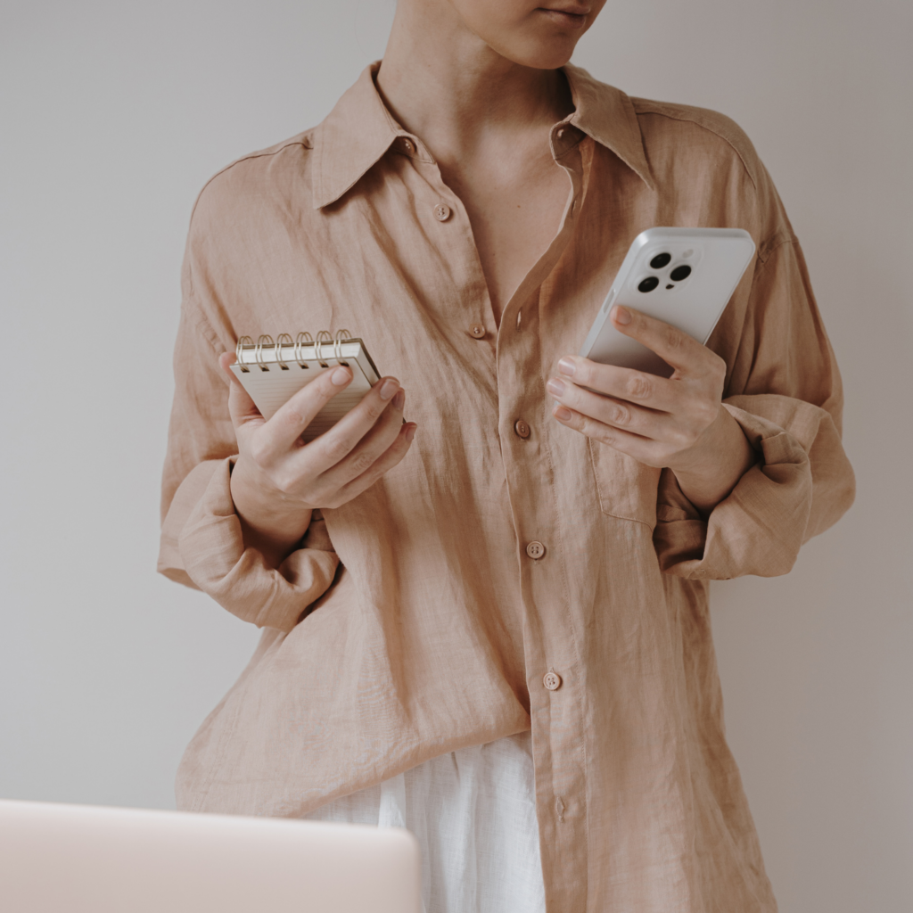 A woman holding her phone and notebook, planning her day and confidently setting boundaries as part of holiday self-care for moms.