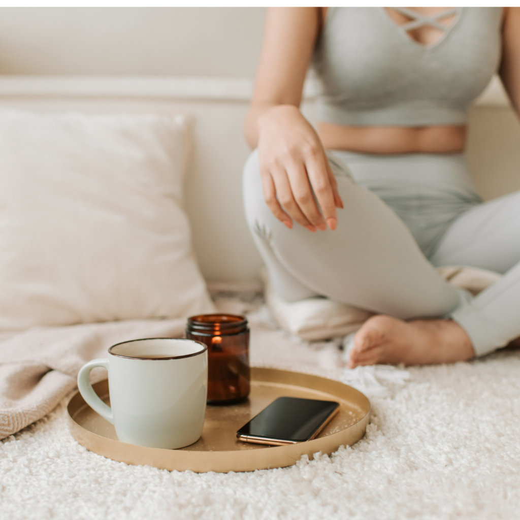 A woman meditating at home with a cup of tea and a lit candle, creating a moment of mindfulness and holiday self-care for moms.