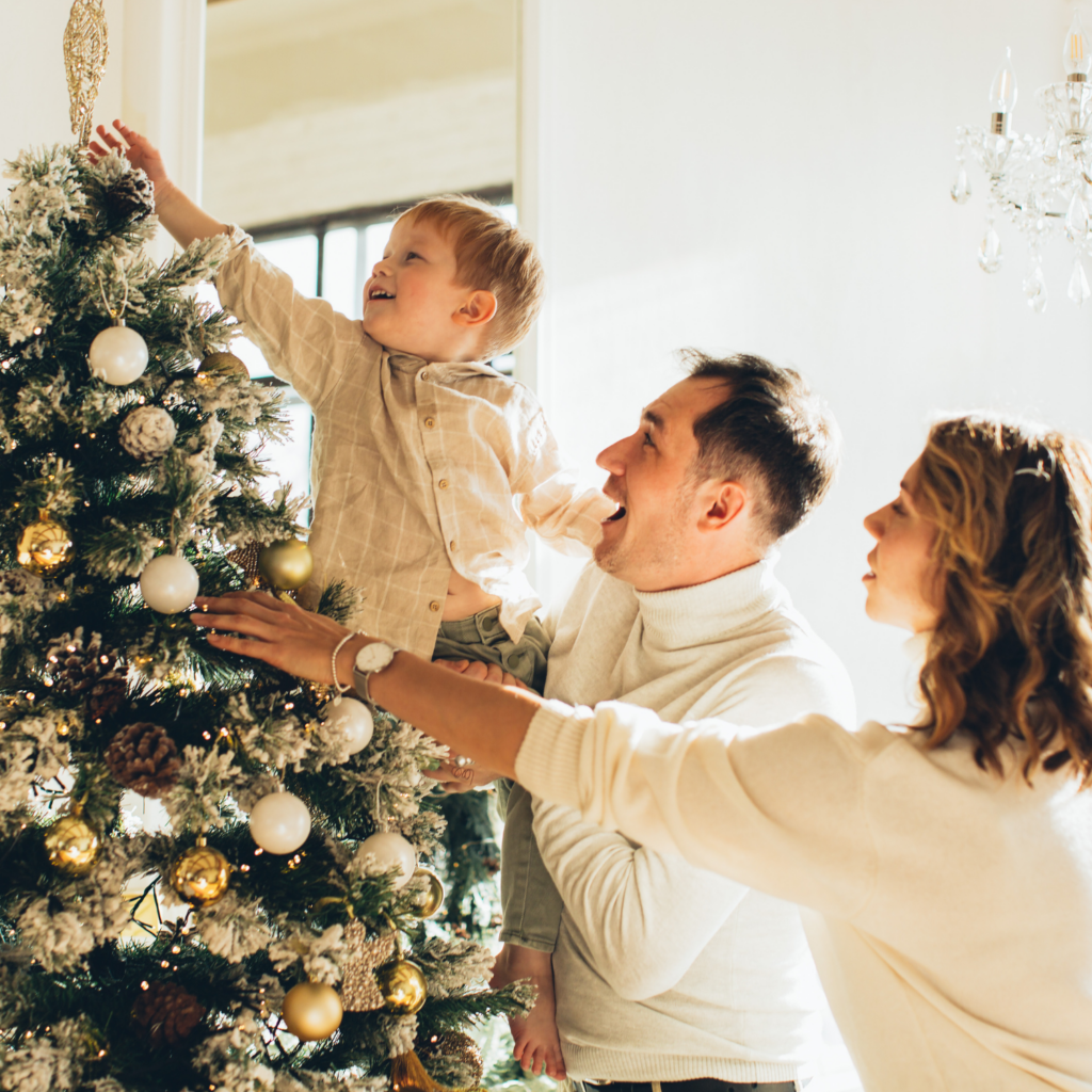 A family joyfully decorating a Christmas tree, sharing responsibilities and embracing holiday self-care for moms.