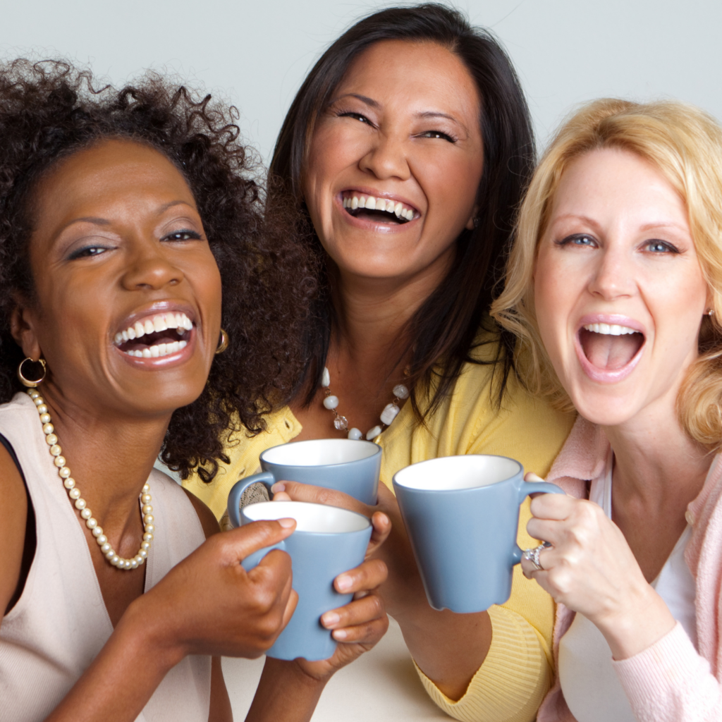 Three moms laughing and toasting their coffee mugs, enjoying connection and supporting each other as part of holiday self-care for moms.