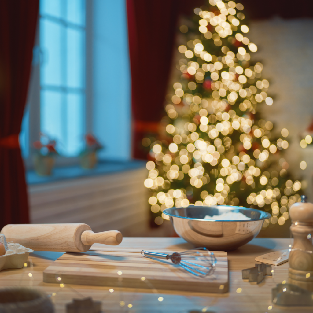 A kitchen decorated for the holidays with festive touches and a lit Christmas tree glowing in the background.