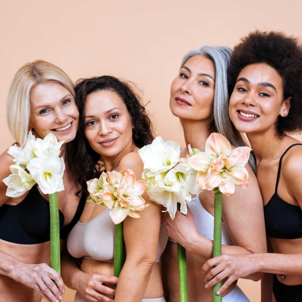 Four women of different ages posing with flowers, celebrating body positivity and the benefits of fasting for energy and hormones.