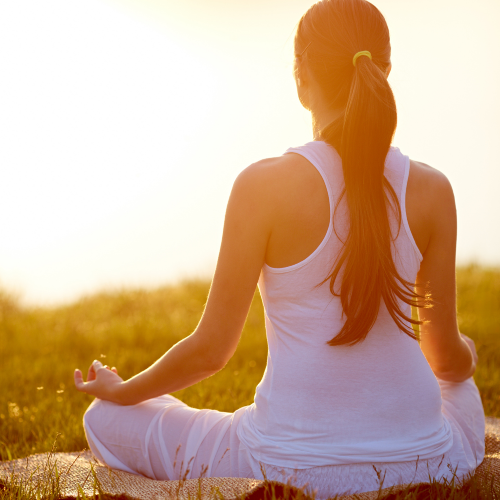 Woman meditating outside in the sun, symbolizing peaceful, hormone-aligned living during midlife