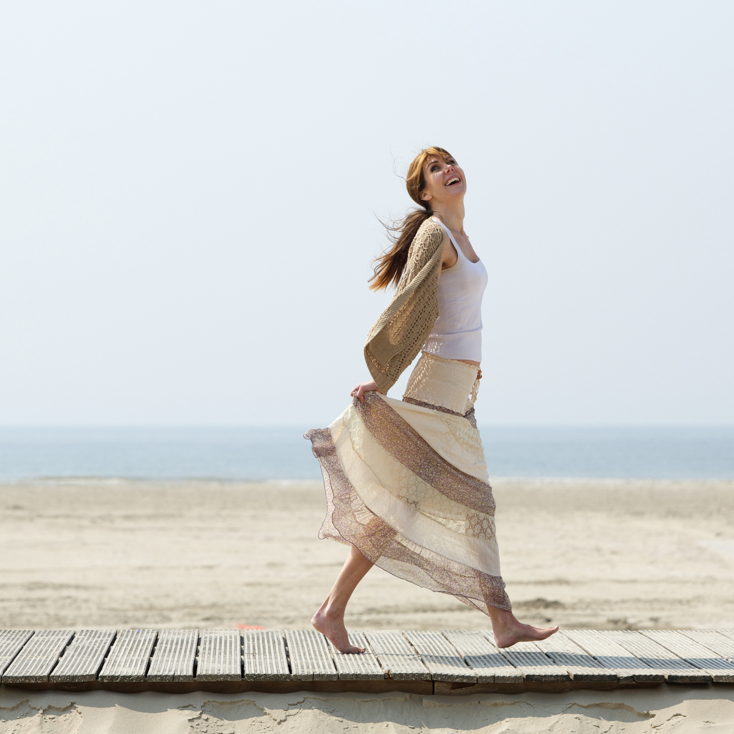 Joyful midlife woman at the beach, representing the energy, clarity, and confidence that comes from cycle syncing in midlife