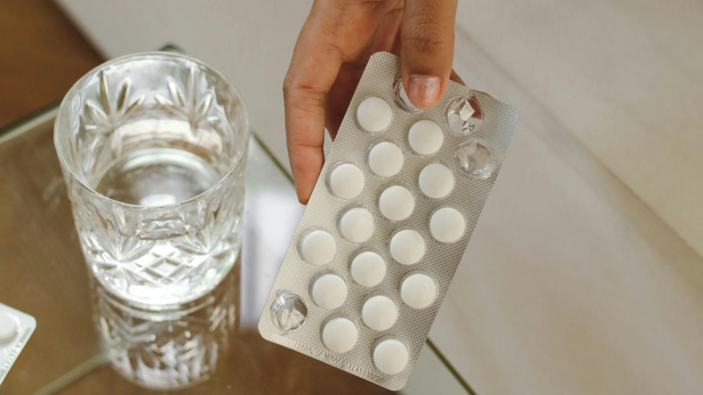 Hand holding hormone therapy tablets beside a glass of water for menopause treatment after 50