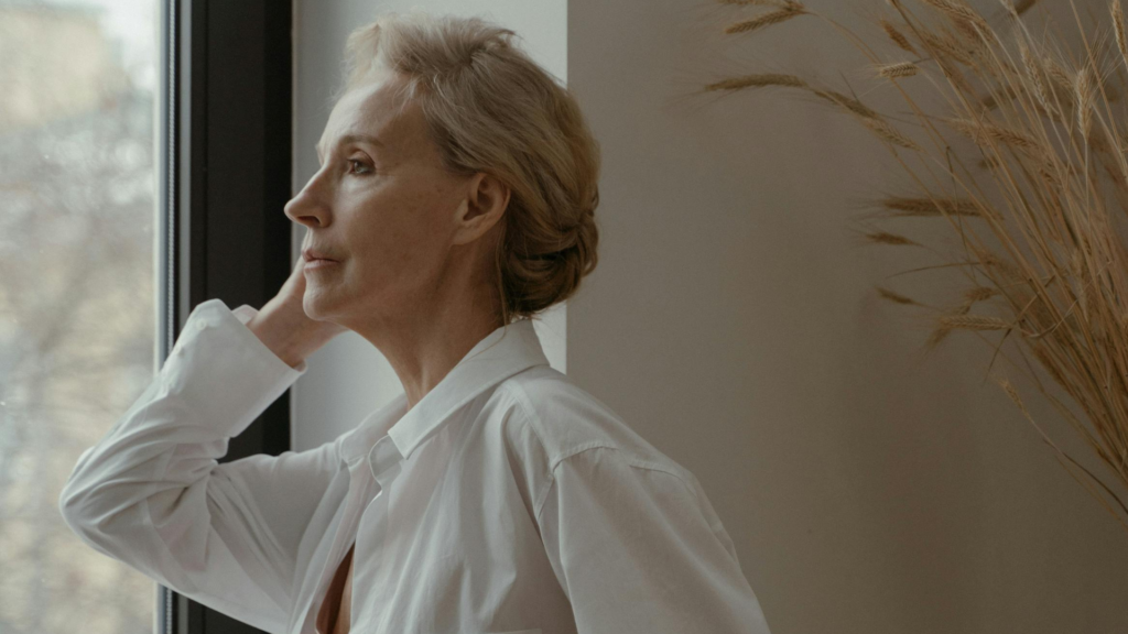 Woman over 50 reflecting by a window while considering hormone therapy options during menopause